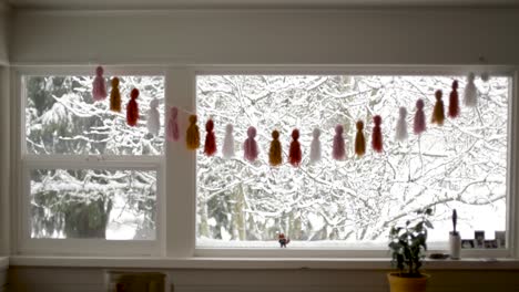 Medium-indoor-shot-of-decorated-window-during-snowy-day-with-snow-covered-trees-outdoors-in-garden
