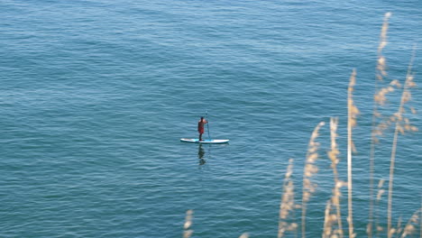 Man-balancing-on-a-stand-up-paddle-board-in-the-tropical-sea,-Portugal