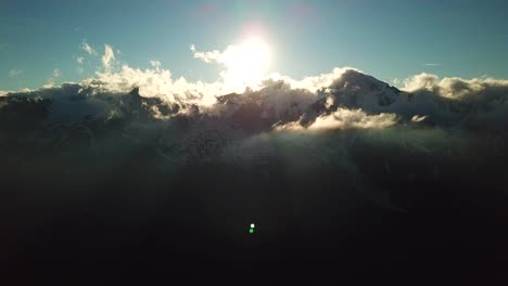 Aerial-view-of-sun-rays-through-a-cloudscape-over-austrian-mountains-snowy-peaks