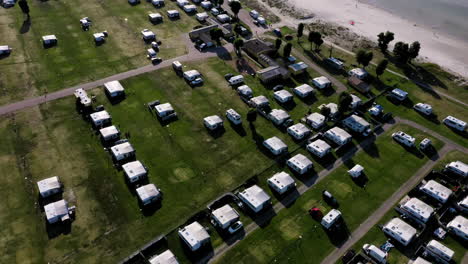 Lots-of-tightly-parked-caravans-camping-at-camp-site-campers-enjoying-holiday-vacation-break-kids-playing-sandy-beach-aerial-drone-birds-view-waves-shore-summer-feeling-happy-relaxed-European-trip-fun