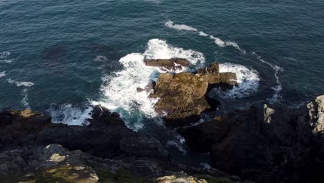 Beautiful-circling-aerial-shot-of-waves-hitting-a-rock-in-the-sea,-Newquay,-Cornwall,-England,-Uk