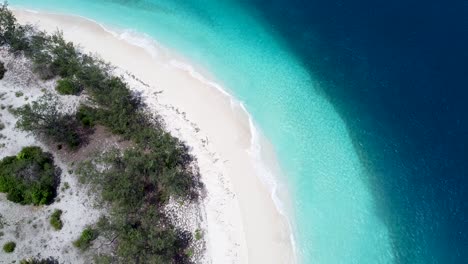 Aerial-drone-birds-eye-view-lowering-towards-stunning-tropical-island-paradise-of-curved-white-sandy-beach-and-crystal-clear-water