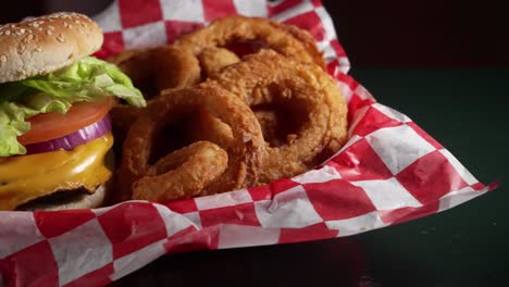 Red-and-blue-light-reflect-off-black-table-top-with-basket-cheeseburger-and-onion-rings,-slider-4K