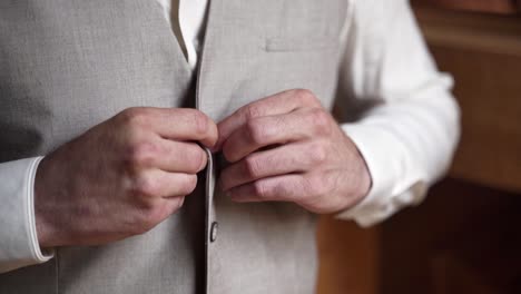 Man-buttoning-up-simple-gray-waistcoat-over-white-shirt,-close-up