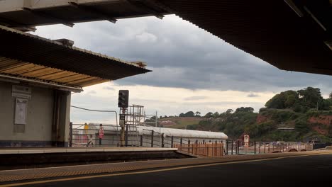 Train-pulls-out-of-Dawlish-Railway-Station,-Devon,-UK-under-a-grey-sky