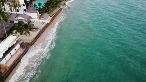 Aerial,-high-rising-sea-levels-crashing-against-tropical-beach-town-seawall
