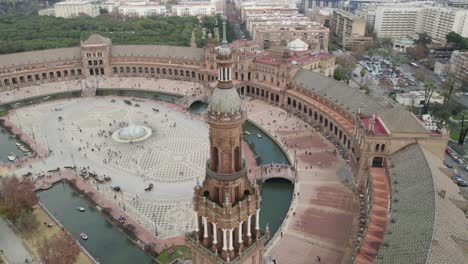 Orbiting-over-Plaza-de-España-tower-revealing-majestic-Square-full-of-tourists,-Seville