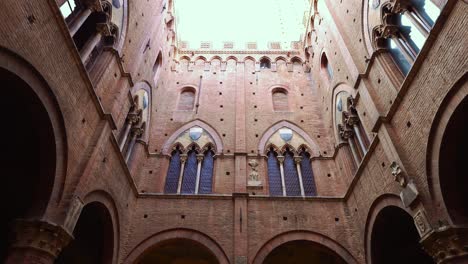 Upward-view-from-the-courtyard-of-the-Palazzo-Pubblico-and-its-Torre-del-Mangia-at-the-shell-shaped-square-Piazza-del-Campo-in-Siena,-Tuscany,-Italy