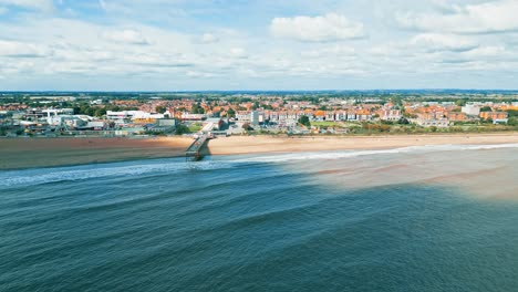 Aerial-drone-video-footage-taken-off-the-Lincolnshire-coast-flying-towards-the-pier-at-Skegness,-with-beach,-blue-sea,-and-shoreline