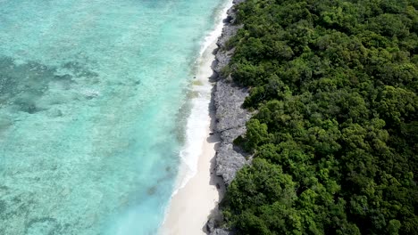 Aerial-drone-of-dense-rainforest-on-uninhabited-remote-tropical-island-with-white-sandy-shoreline-and-idyllic-crystal-clear-turquoise-ocean-water