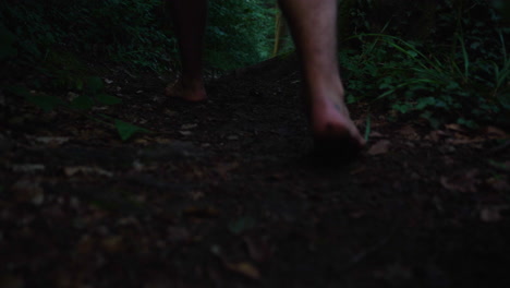 Closeup-of-mans-feet-walking-barefoot-in-slow-motion-down-a-path-in-an-dark-forrest