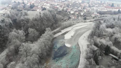 drone-flies-above-clear-river-revealing-Tolmin-town-in-Slovenia-on-winter-morning