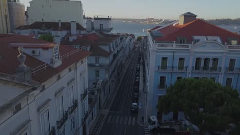Aerial,-descending,-drone-shot,-backwards-over-traffic-and-the-rua-do-alecrim,-surrounded-by-the-city-of-Lisbon,-Portugal,-on-a-sunny-evening