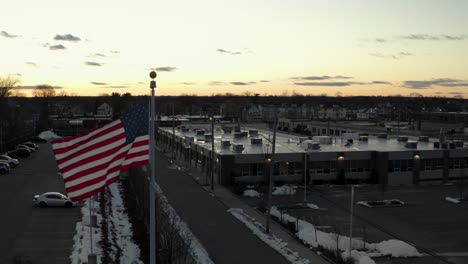 At-dusk,-the-flag-of-the-United-States-of-America-flaps-in-the-gentle-breeze---aerial-view