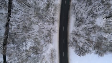 White-vehicle-travels-up-snowy-winter-road,-top-down-drone-view