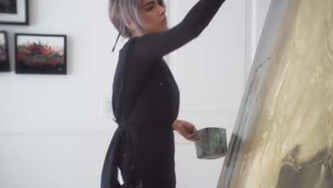 Latina-Artist-Working-With-Large-Paintbrush-Standing-In-Front-Of-Wide-Canvas