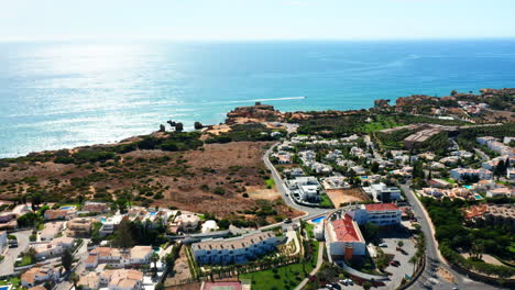 Luftaufnahme-Der-Wunderschönen-Küste-Der-Algarve-Mit-Sonnenlichtreflexion-Im-Meerwasser-Und-Hotelresorts-Mit-Pool-In-Portugal