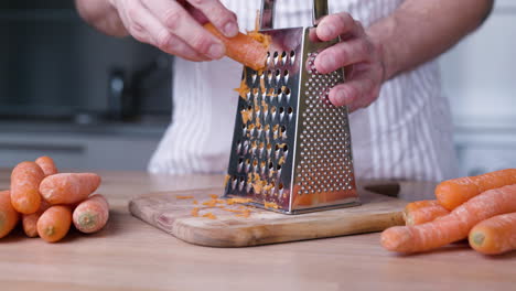 Nahaufnahme-Von-Hand,-Die-Karotten-Auf-Der-Reibe-Für-Karottenkuchen-In-Der-Küche-Reibt