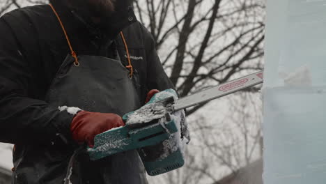 Ice-sculptor-using-electric-chainsaw-to-cut-details-on-face-of-ice-blocks-in-falling-snow,-Slow-Motion
