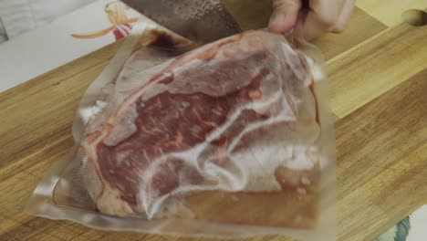 Chef-drops-meat-steak-in-vacuum-package-on-the-cutting-board-and-opens-it