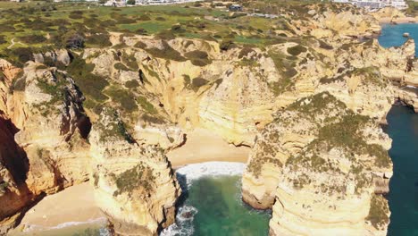 Secluded-Pinheiros-Beach-surrounded-by-jagged-rock-formations-in-Lagos,-Algarve,-Portugal---Aerial-Fly-back-Tilt-up-shot