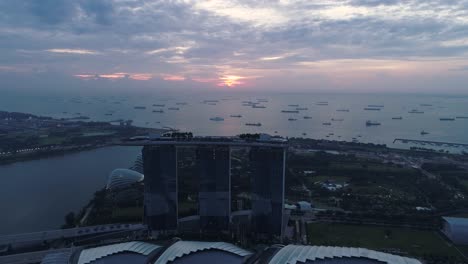 Marina-Bay-Sands-hotel-at-sunrise-with-distant-boats-near-shore,-aerial