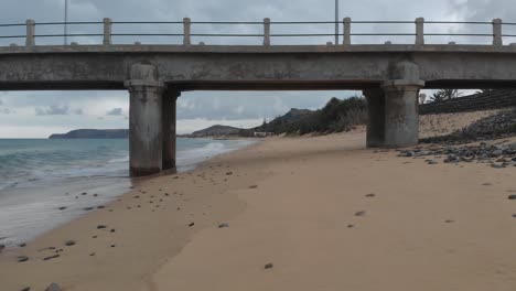 First-person-shot-along-sandy-beach-and-under-pylon-of-pier