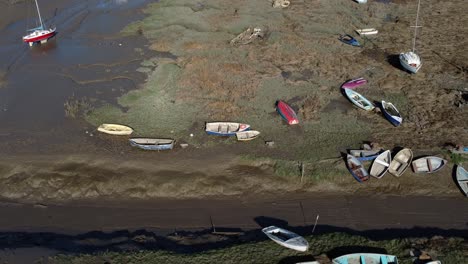 Various-moored-fishing-boat-wreck-shipyard-in-marsh-mud-low-tide-coastline-aerial-view-push-in-tilt-down