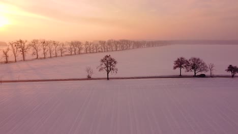 Light-morning-traffic-on-a-local-road-through-snow-covered-fields-at-sunrise