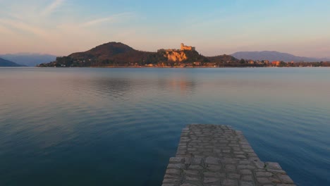 Peaceful-scene-of-concrete-pier-on-lake-Maggiore-calm-water-in-Italy,-Angera-castle-on-background