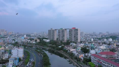 Fly-in-drone-shot-of-buildings,-Sunset,-bridge,-canal,-reflection-and-urban-sprawl-of-Ho-Chi-Minh-City-District-Eight
