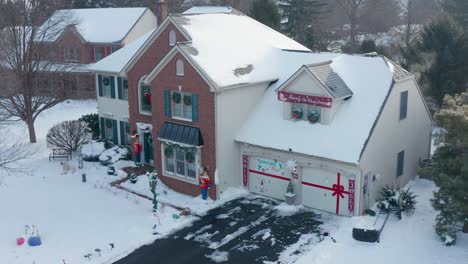 Aerial-of-front-exterior-of-house-covered-in-snow,-decorated-for-Christmas