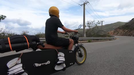 Man-rides-motorbike-transporting-surfboard-and-kitesurfing-equipment
