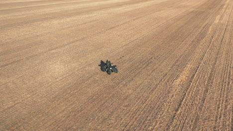 Person-drives-atv-in-the-middle-of-farm-field,-aerial-reveal