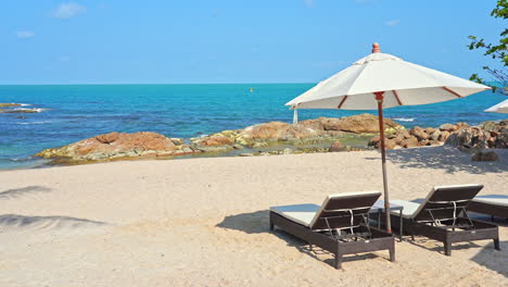 Two-empty-sun-loungers-under-a-sun-umbrella-facing-a-picturesque-sandy-beach-and-ocean-view