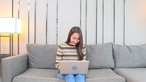 An-attractive-young-woman-sitting-on-a-couch-inputs-data-into-her-laptop