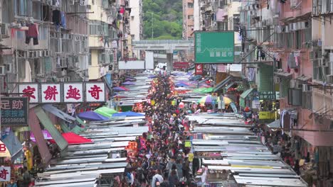 Tilting-clip-of-Fa-Yuen-street-market-stalls-as-large-crowds-of-shoppers-look-for-bargain-priced-vegetables,-fruits,-gifts,-and-fashion-goods-in-Hong-Kong