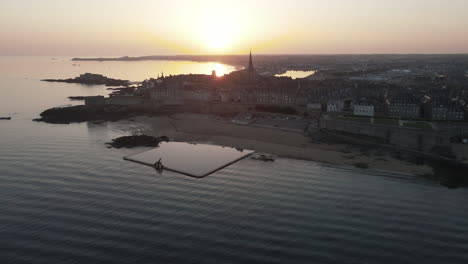 Saltwater-pool-on-beach-at-dusk-with-Saint-Malo-old-city-in-background,-Plage-de-Bon-Secours,-France