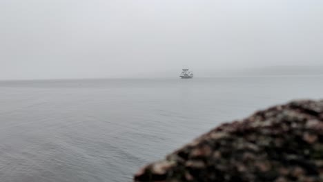 Norwegian-ferryboat-Hjellestad-crossing-fogg-fjord-Leroyosen-in-reduced-visibility-outside-Bergen-Norway---Cinematic-clip-with-blurred-sea-rock-in-foreground