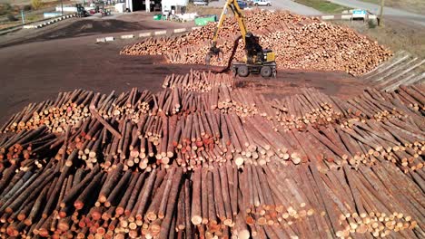 pan-right-wide-drone-shot-of-a-log-loader-at-a-sawmill-moving-logs-on-wood-piles-in-a-desert-environment