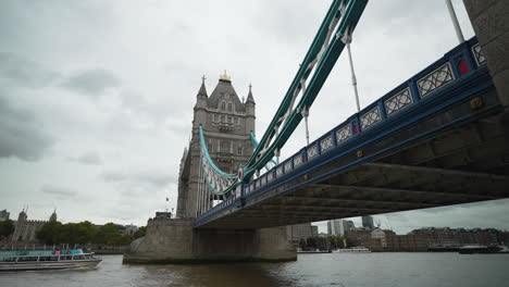 Boats-ride-the-River-Thames-underneath-Tower-Bridge-in-London-on-a-cloudy-day