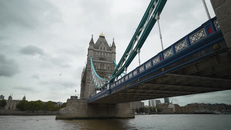 Wide-angle-of-boats-driving-under-the-Tower-Bridge-in-London-on-the-River-Thames-on-a-cloudy-day