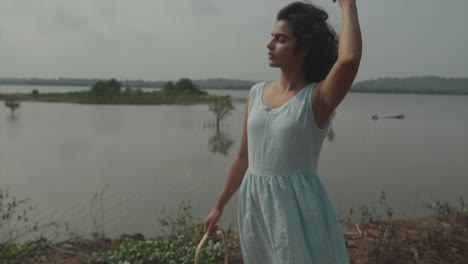 Static-slow-motion-shot-of-an-elegant-and-stylish-indian-woman-in-turquoise-dress-stroking-through-her-black-hair-during-windy-weather-in-front-of-a-lake-with-sea-islands-in-100-fps