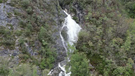Waterfall-cascading-though-trees-Lake-Bohinj-Slovenia-drone-aerial-push-in-shot