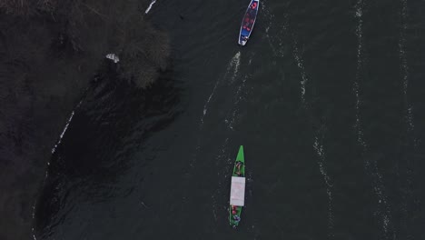 Drohnenansicht-Von-Oben-Auf-Ein-Blaues-Boot-Und-Ein-Grünes-Boot,-Das-Einen-Fluss-Hinunter-Segelt