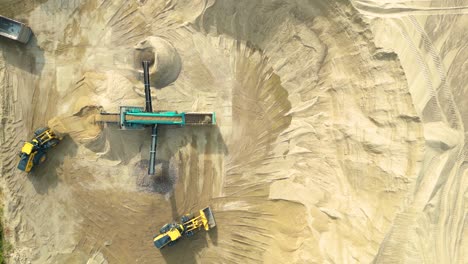 Wheel-loader-with-bucket-in-front-load-stone-in-crusher,-aerial-drone-shot