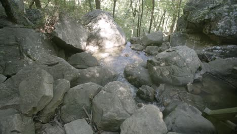 Slow-motion-wide-shot-of-a-small-stream-meandering-through-a-group-of-rocks-and-boulders