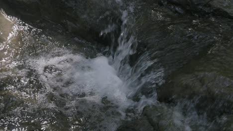 Close-up-slow-motion-footage-of-a-small-waterfall-coming-off-a-rock-in-a-stream