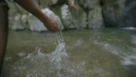 Slow-motion-footage-following-the-hands-of-a-young-african-american-man-as-they-go-through-the-water-of-a-stream