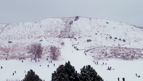 Aerial-shot-of-kids-playing-on-a-snow-covered-hill-in-winter